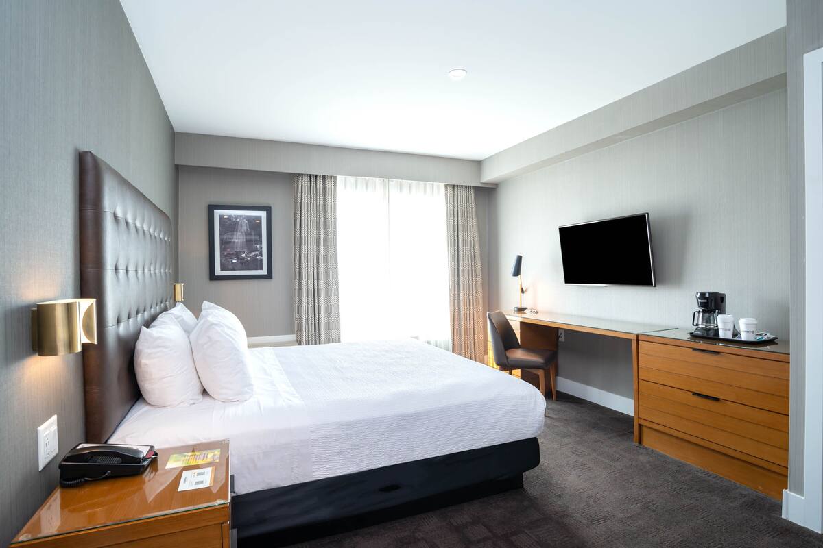 Habitación de hotel con una cama grande, un escritorio, una silla, un televisor de pantalla plana y una cafetera.