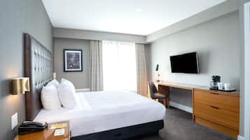 A hotel room with a large bed, a desk, a chair, a flat-screen TV, and a coffee maker.