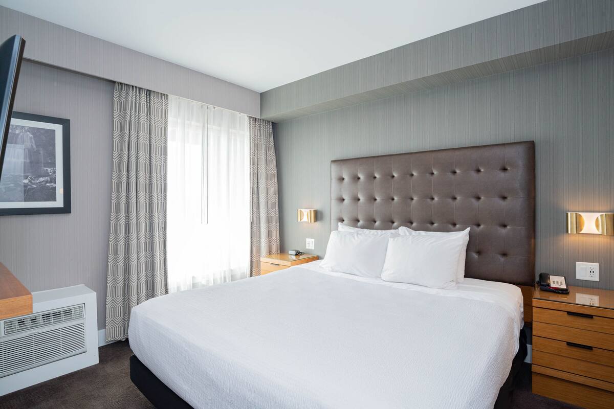 Habitación de hotel con una cama grande, una mesita de noche, una lámpara de pared y un cuadro en la pared.