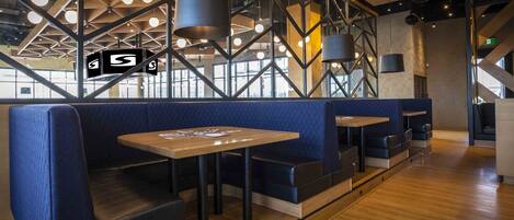 A modern restaurant interior with blue cushioned booths, wooden tables, and pendant lighting.