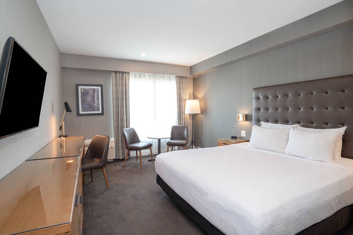 Una habitación de hotel con una cama grande, un escritorio, dos sillas, un televisor y una ventana con cortinas.