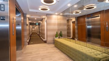 Un moderno vestíbulo de hotel con un largo pasillo, ascensores, un banco acolchado verde y un mostrador de recepción de madera.