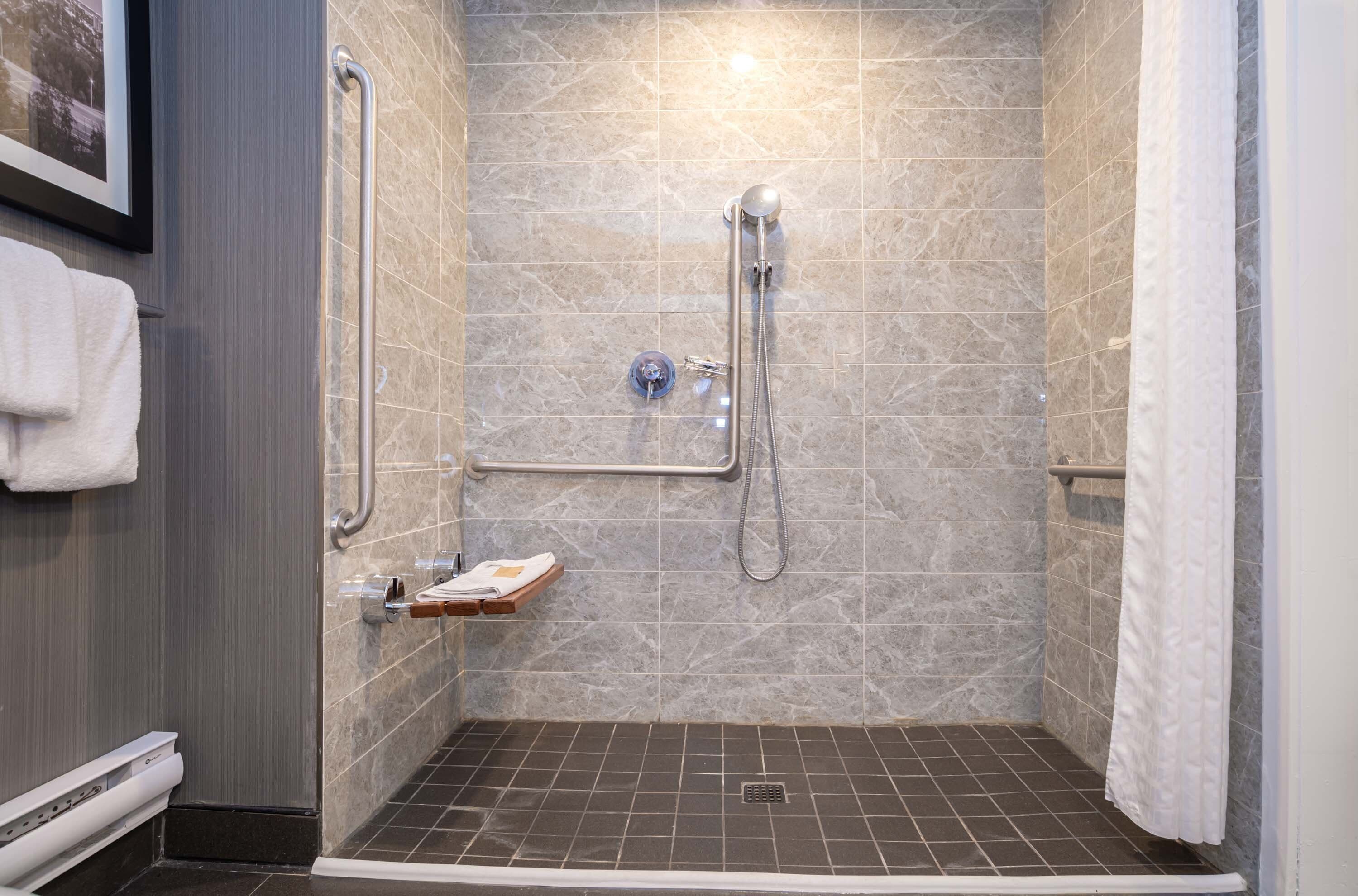 A walk-in shower with a handrail, a grab bar, and a shelf with toiletries.