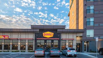 Un restaurante Denny's con tres coches aparcados frente a él, un cartel de estacionamiento y un cielo despejado con nubes.