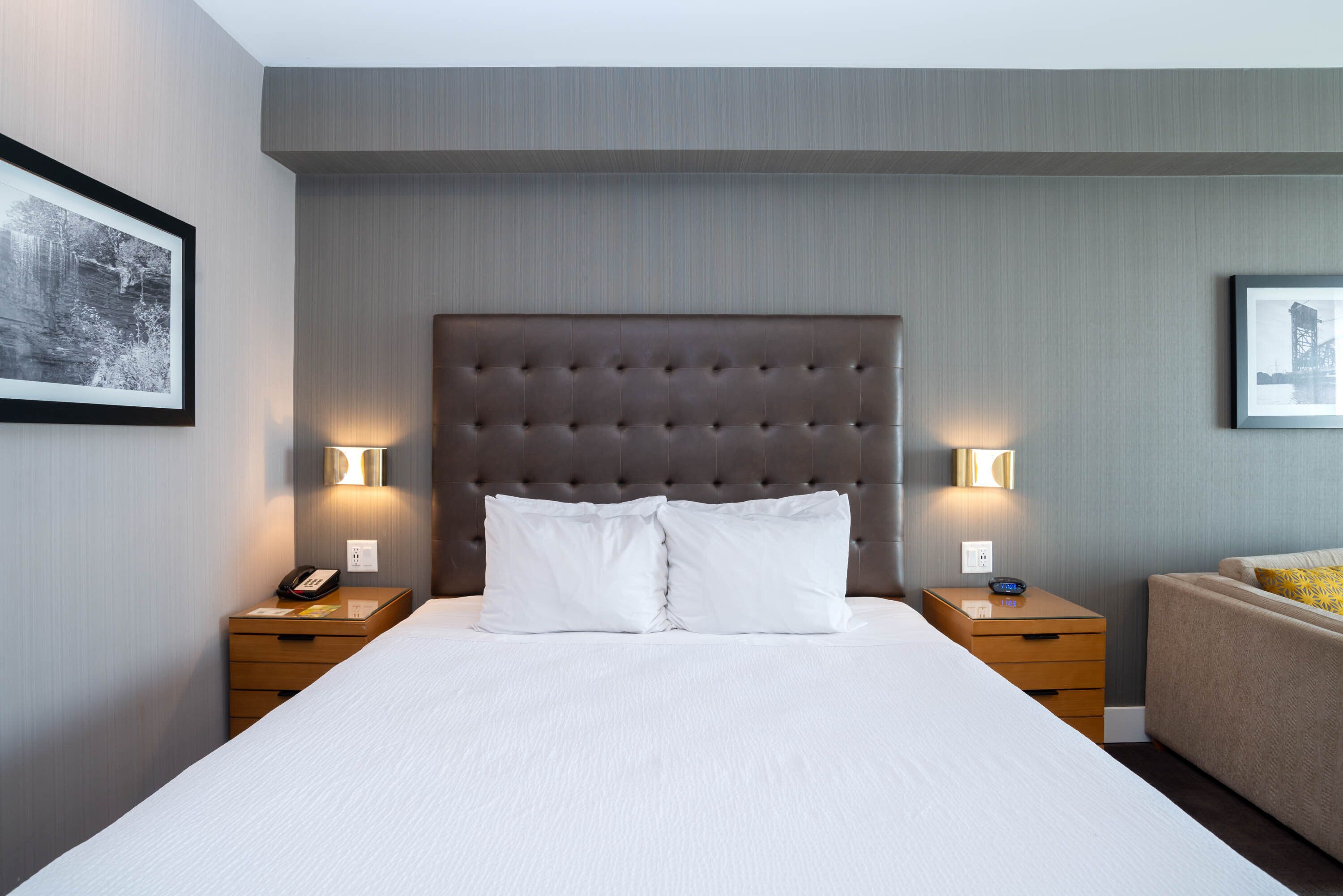 A neatly made bed with white linens, two bedside tables with lamps, and framed pictures on the walls.