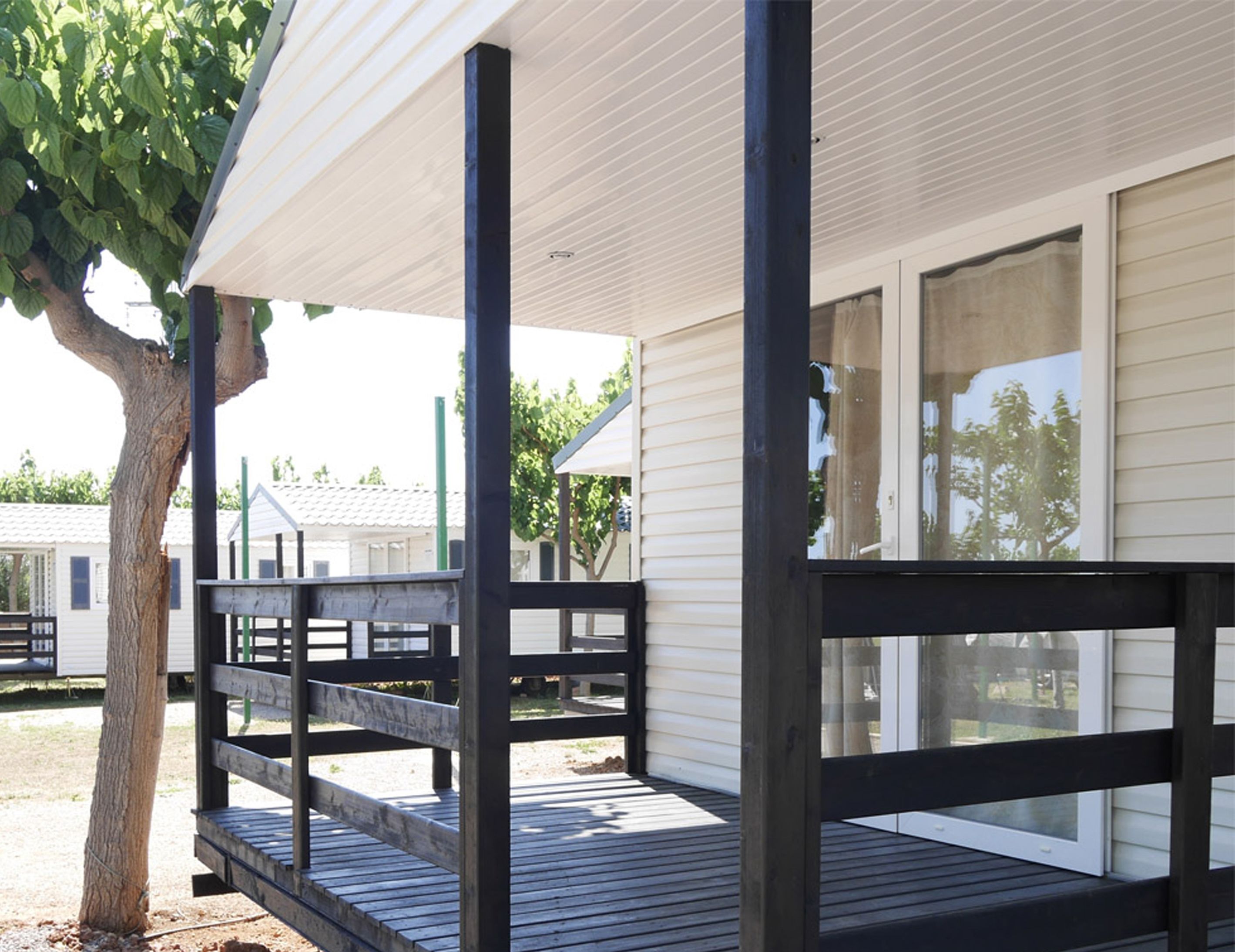 A covered porch with a wooden railing, a tree, and a building with large windows.