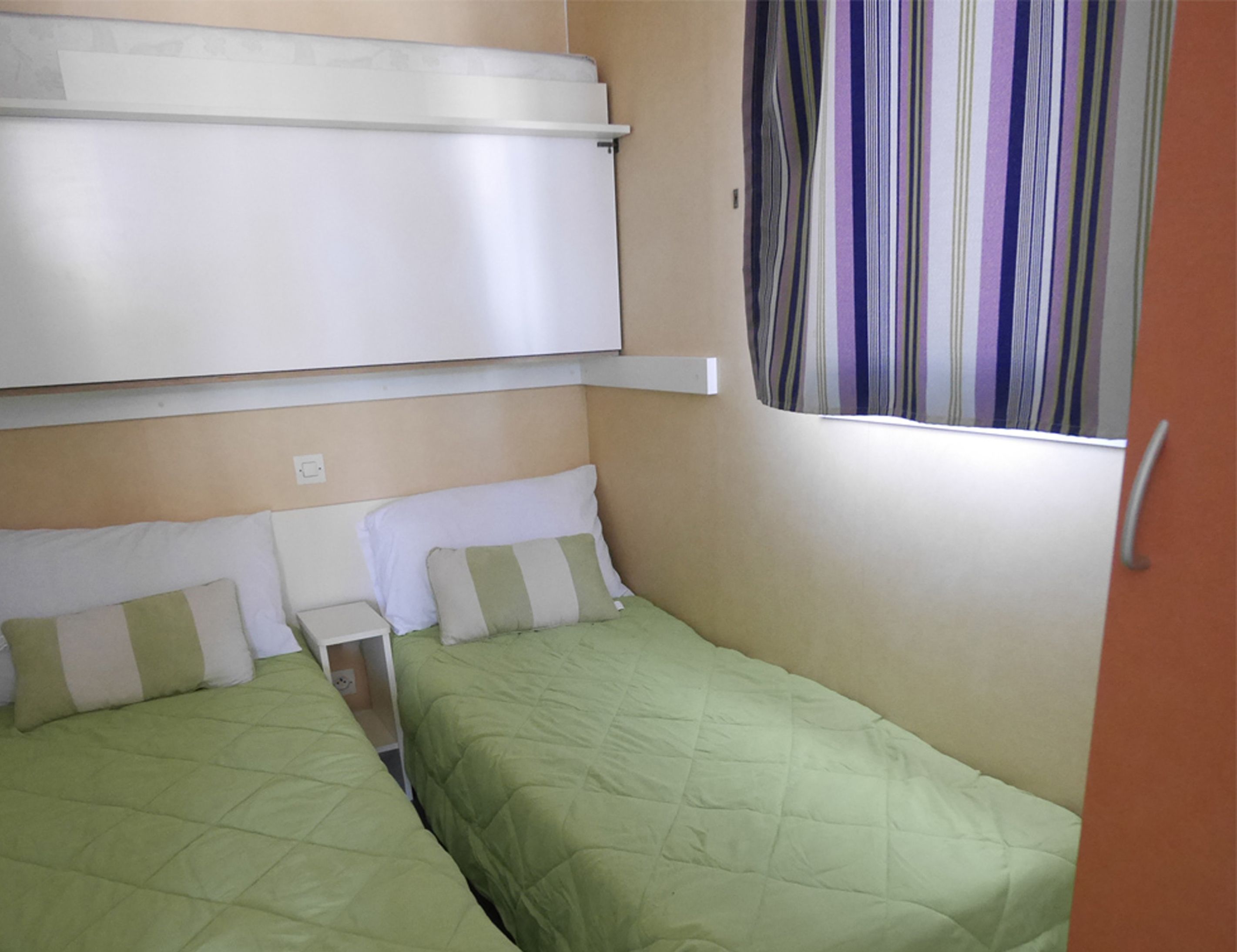 A compact room with two single beds, a window with striped curtains, and a white headboard.