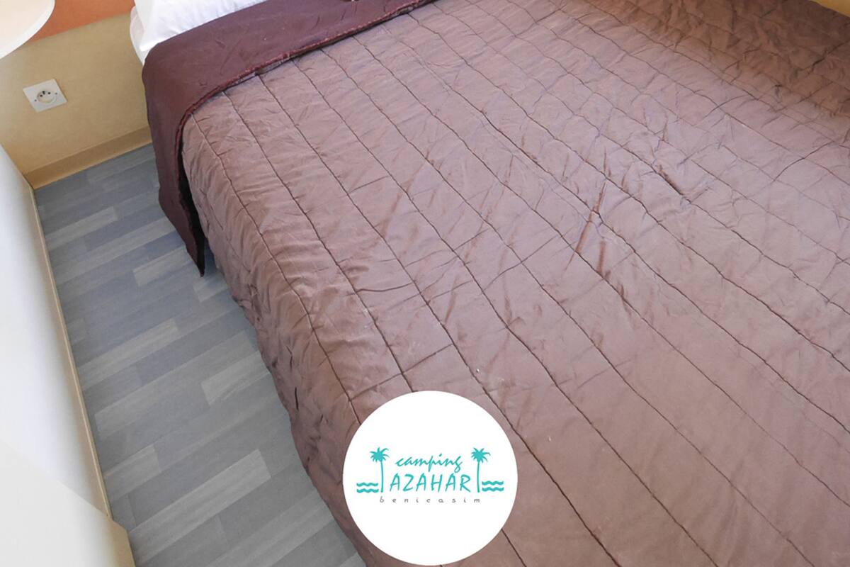 A neatly made bed with a brown bedspread and a striped pillow.