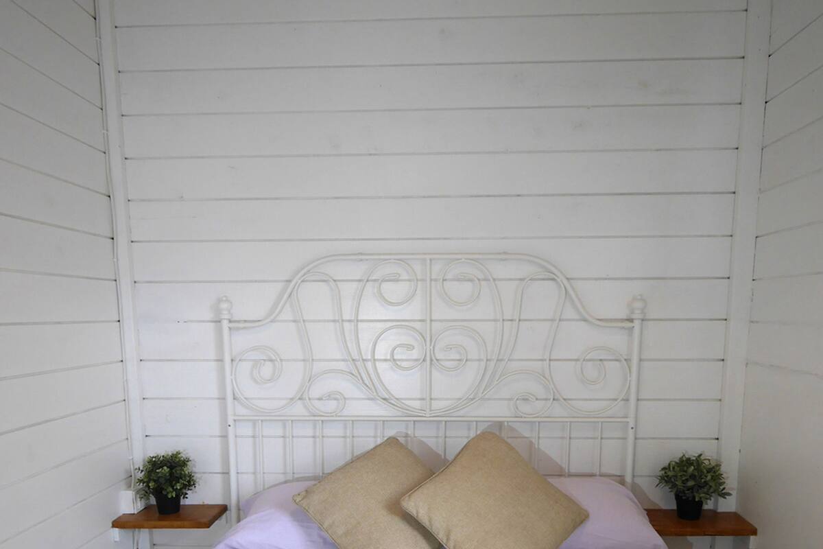 A bed with a white metal headboard, two bedside tables with small potted plants, and two beige pillows.