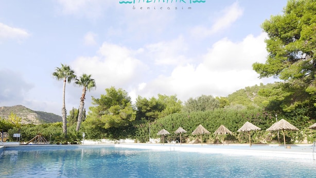 A clear blue swimming pool with palm trees and thatched umbrellas in the background. - Camping Azahar (Benicassim)