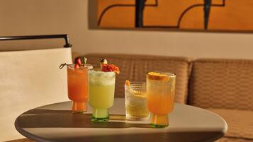 A round table with four drinks, each with a different garnish, in a room with a couch and a painting on the wall.