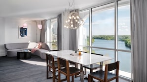 A modern hotel room with a large window offering a view of a river and buildings. There is a dining table with chairs, a sofa, and a lamp. - The LINE Austin (Austin)
