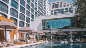 A swimming pool with lounge chairs and umbrellas, surrounded by modern buildings with large windows. - The LINE Austin (Austin)