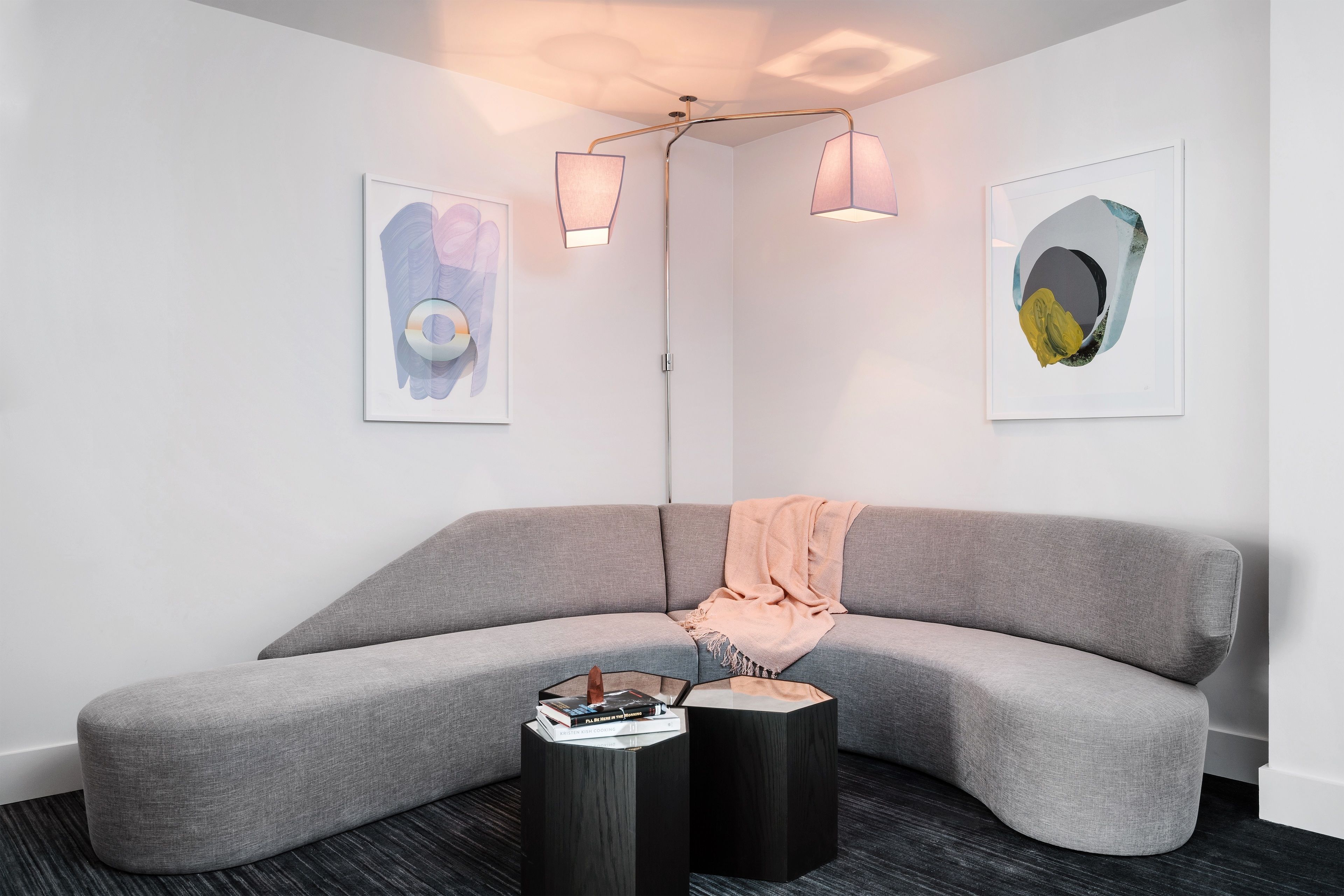 Una sala de estar moderna con un sofá seccional gris, dos mesas auxiliares negras y obras de arte abstractas en las paredes.