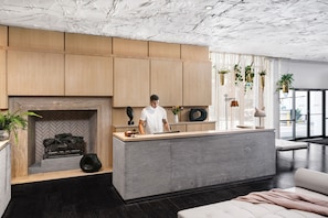 A modern kitchen with a central island, wooden cabinets, a fireplace, and hanging plants.