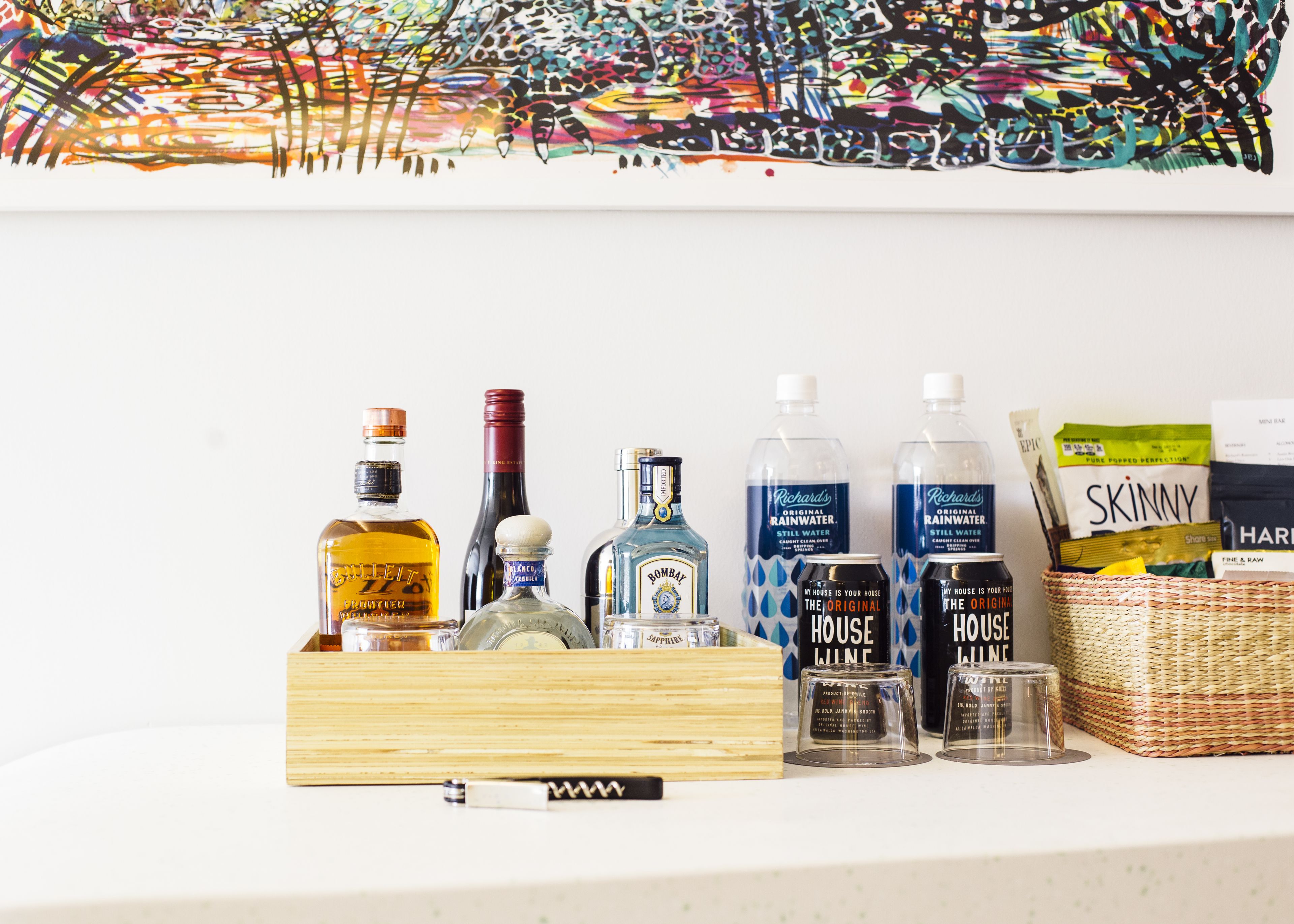 A variety of alcohol bottles and a basket of snacks on a shelf.