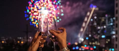 Two hands holding wine glasses with a colorful fireworks display in the background.