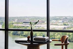 A table with a vase, books, and a chair by a window overlooking a cityscape.