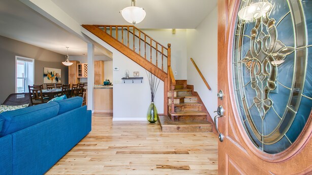 Ein geräumiges Wohnzimmer mit einer Holztreppe, einem blauen Sofa und einem Essbereich im Hintergrund.