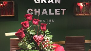Zona de recepción de un hotel con un cartel que dice "GRAN CHALET HOTEL" y un ramo de rosas rojas sobre una mesa.