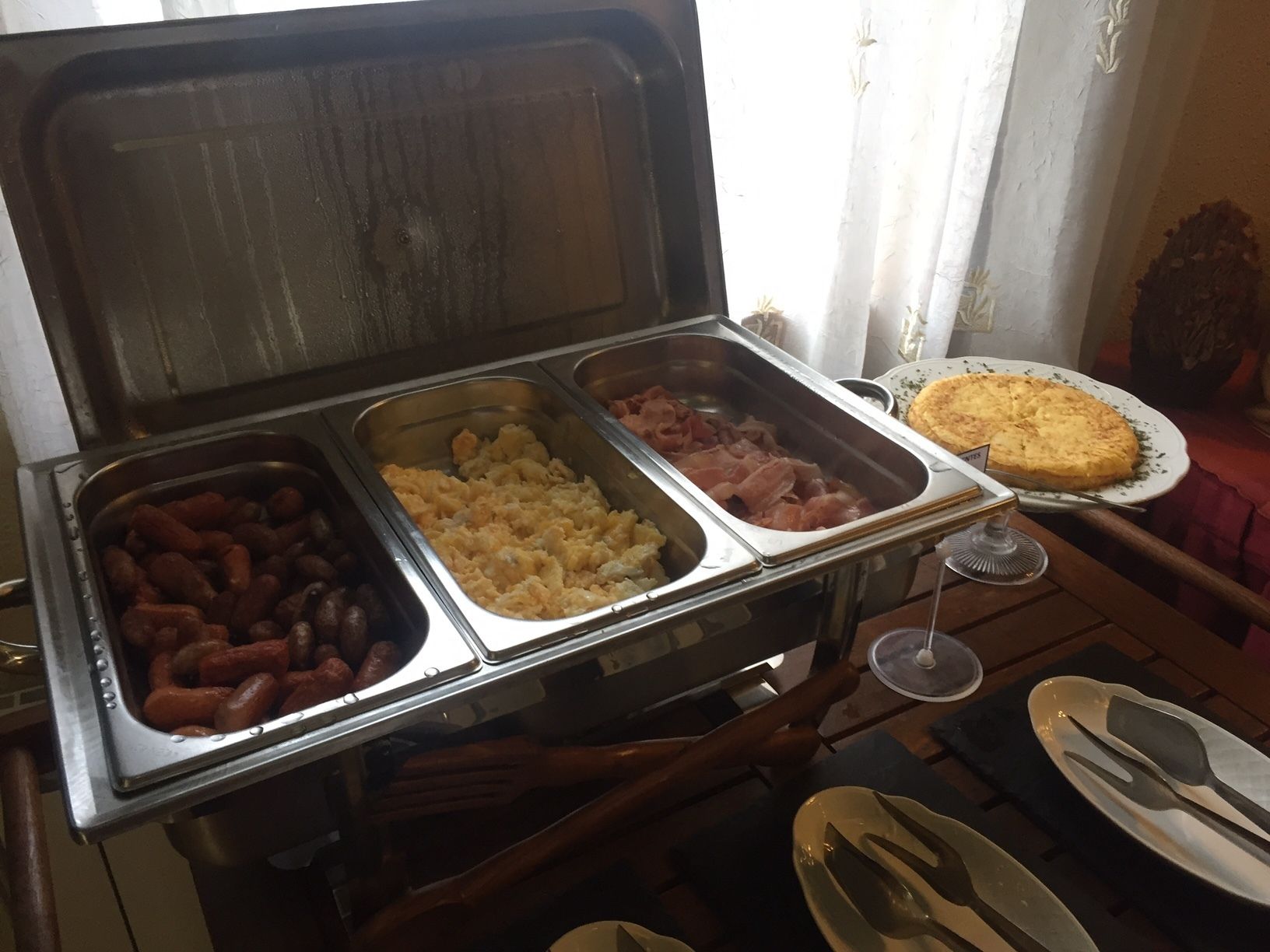 Ein reichhaltiges Buffet mit verschiedenen Speisen, darunter Würstchen, Rührei und Schinken.