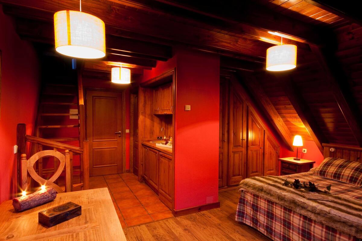 Un dormitorio acogedor en el ático con una escalera de madera, una pequeña cocina y una cama con ropa de cama de cuadros.