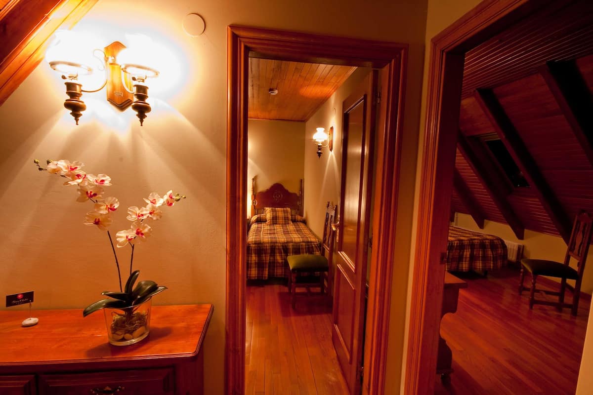 Un pasillo con un escritorio de madera, una orquídea en maceta y una cama con colcha escocesa al fondo.