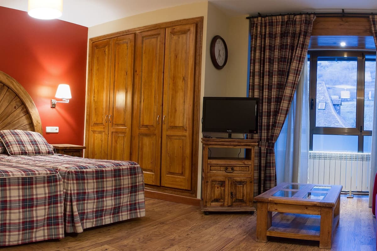 Una habitación con dos camas, un armario de madera, un televisor y una ventana con cortinas.
