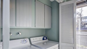 A laundry room with a front-loading washer and dryer, white cabinets, and a window with blinds. - The East End Retreat (Boise)
