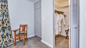 A room with a wooden chair, a wardrobe, and a closet with hanging clothes. - The East End Retreat (Boise)