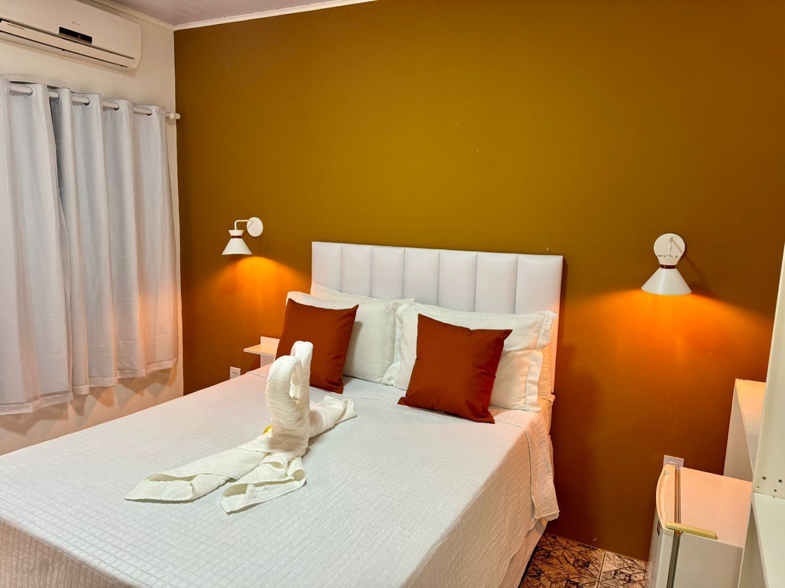 Una cama bien hecha con sábanas blancas y almohadas marrones, un cabecero blanco y dos lámparas de noche.