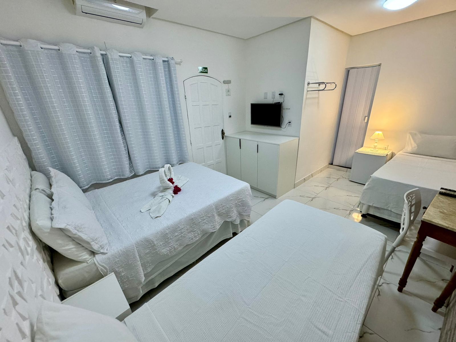 A hotel room with two beds, a TV, a desk, and a bathroom.