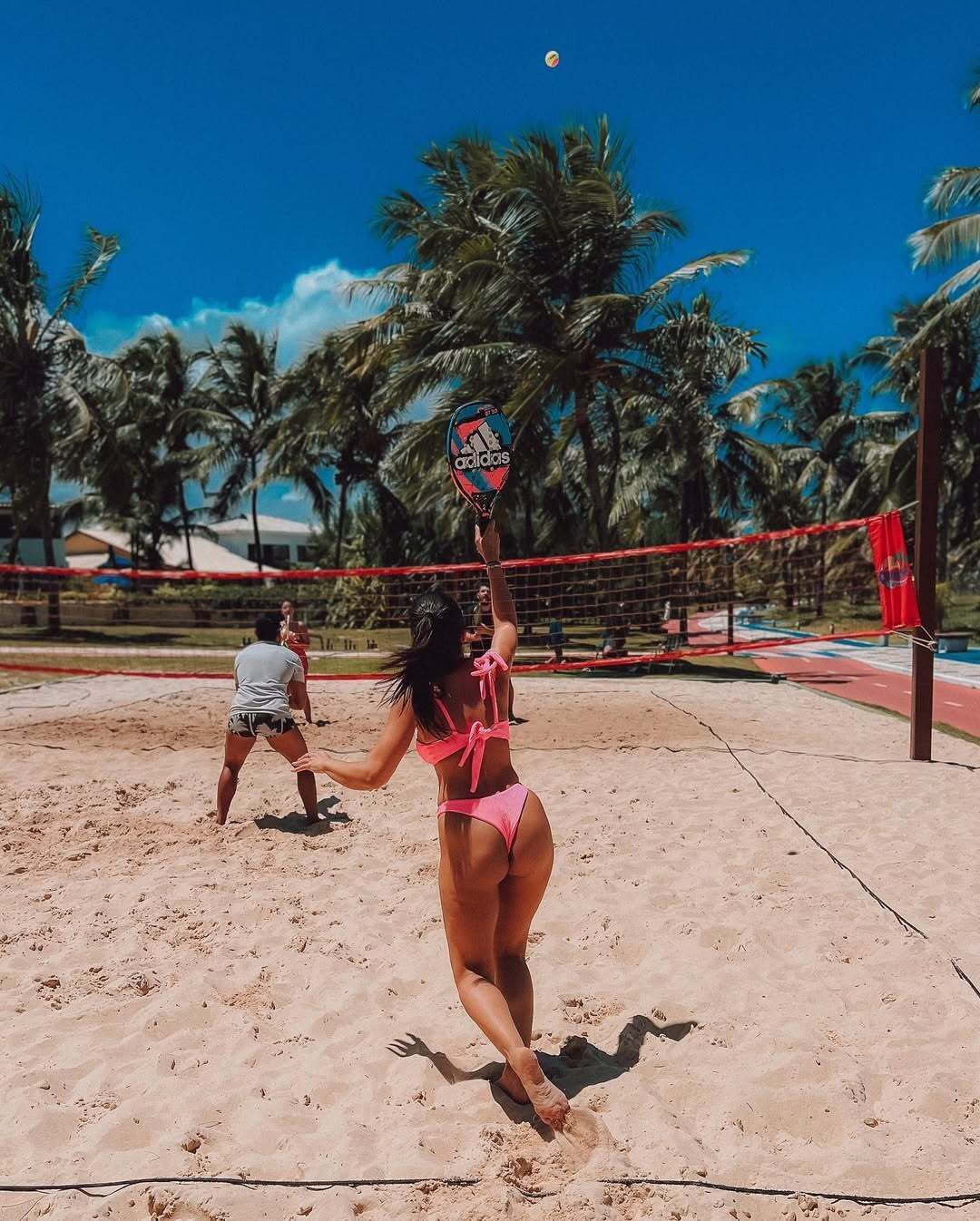 Ένας αγώνας beach volley με δίχτυ και φοίνικες στο φόντο.