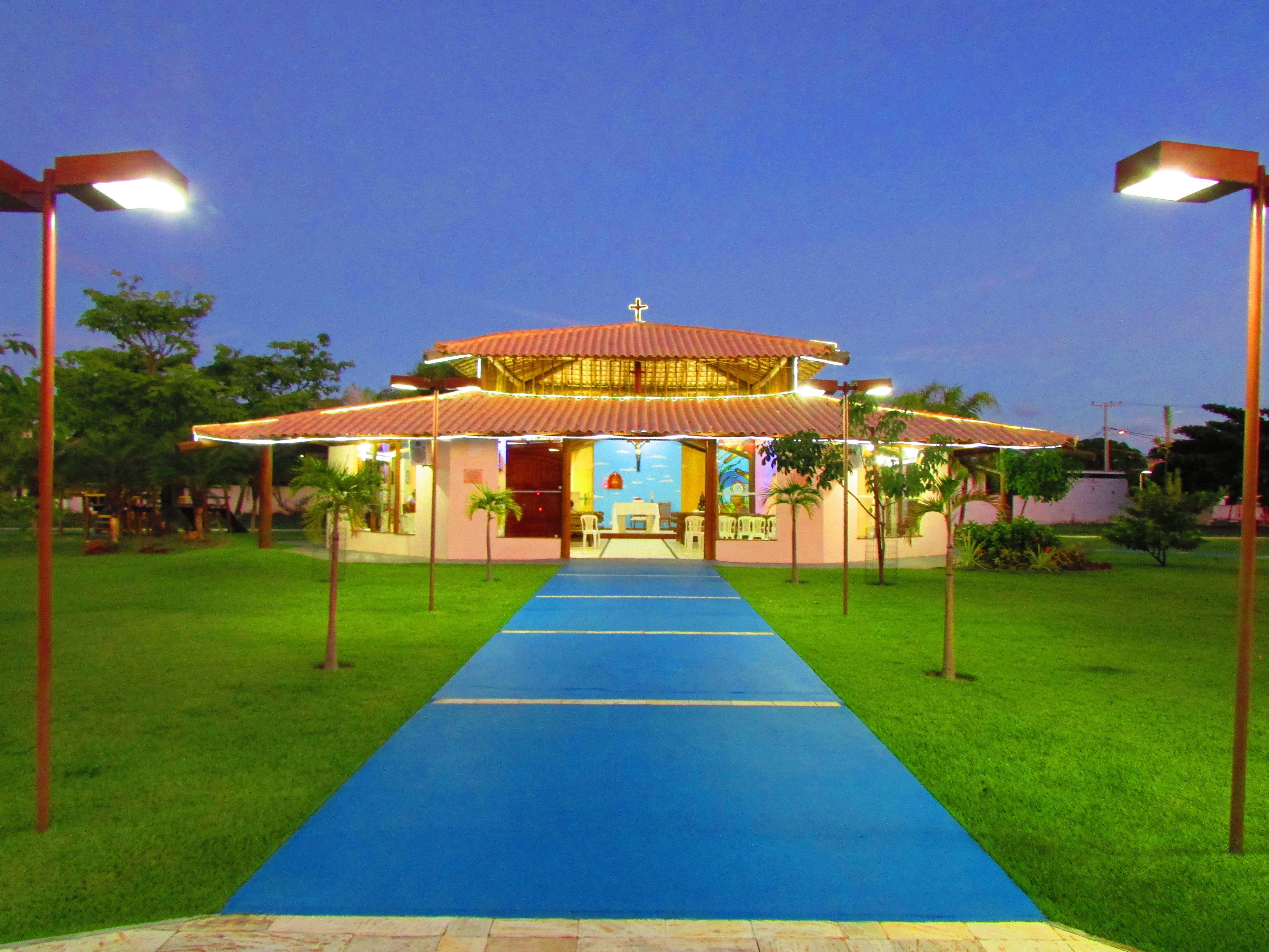 A building with a blue pathway leading to a covered entrance, surrounded by grass and palm trees.