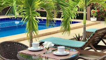 Un espacio para comer junto a la piscina, con sillas de mimbre, una mesa de vidrio y una piscina al fondo.
