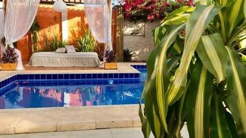 A pool area with a sunlit outdoor seating area, a tiled pool, and lush greenery.