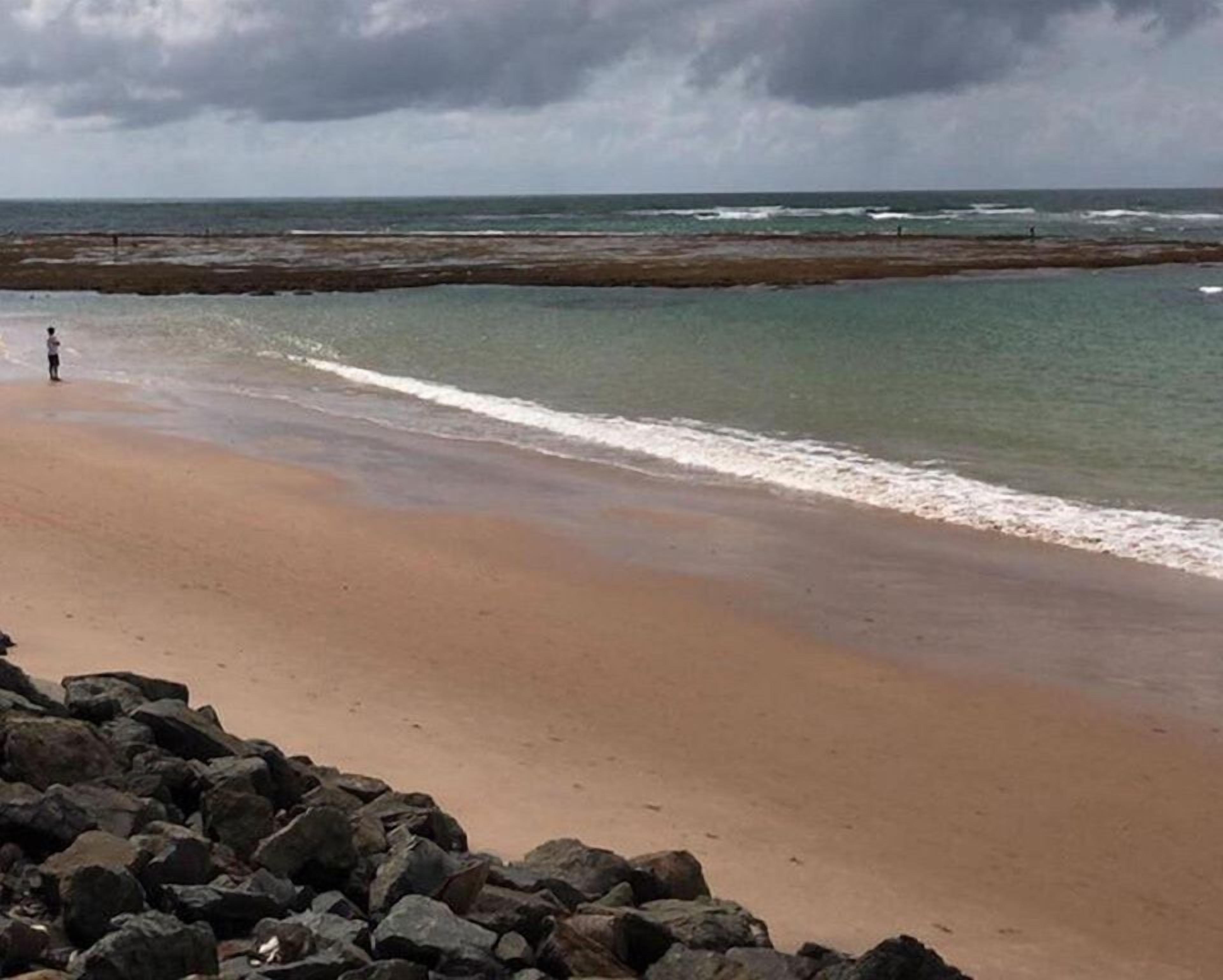 A beach with a rocky foreground and a person standing near the water's edge.