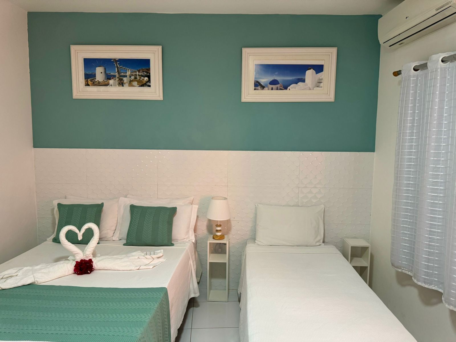 Une chambre d’hôtel avec deux lits, des murs de couleur turquoise, des têtes de lit blanches et deux tableaux représentant un paysage côtier.