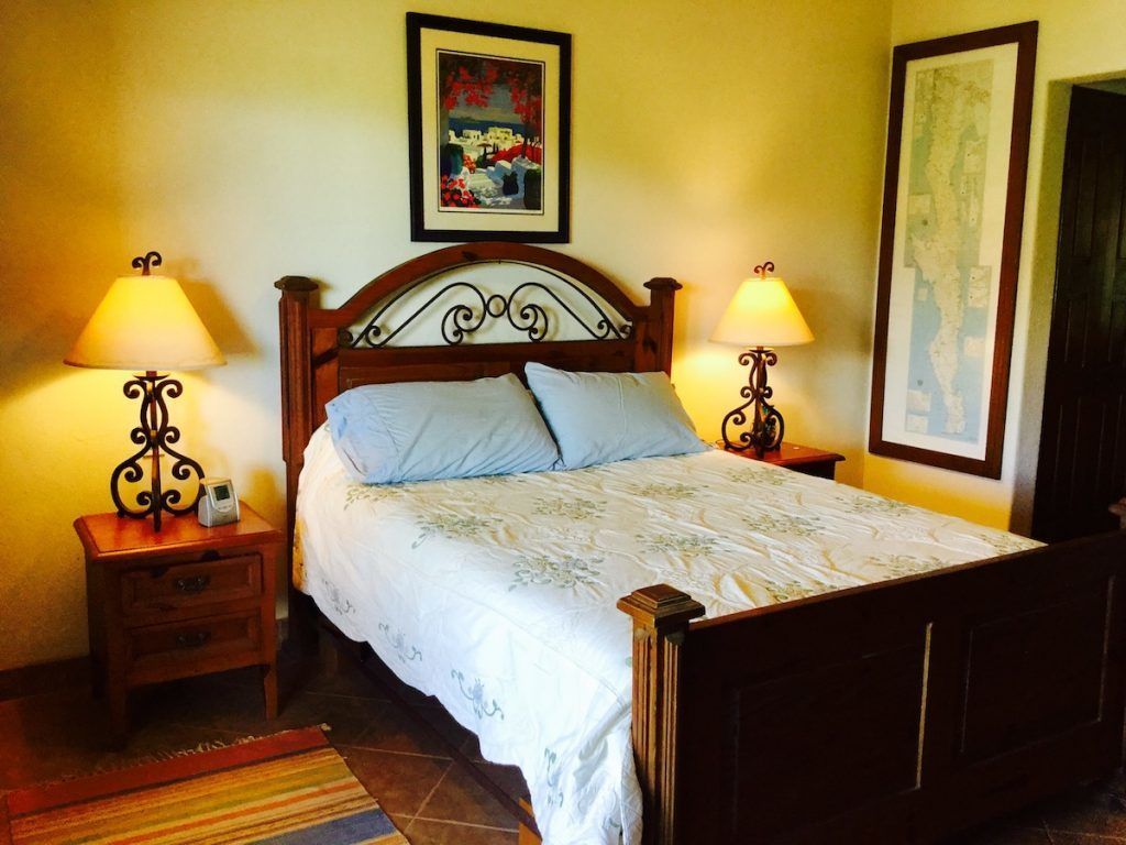 A neatly made bed with a wooden headboard, two bedside tables with lamps, a framed picture above the bed, and a map on the wall.