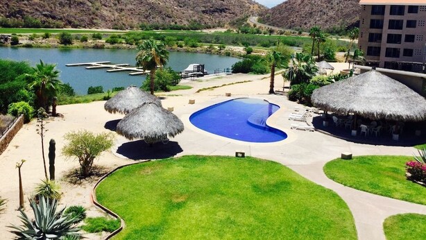 A resort with a swimming pool, thatched-roof structures, and a view of mountains and a lake.