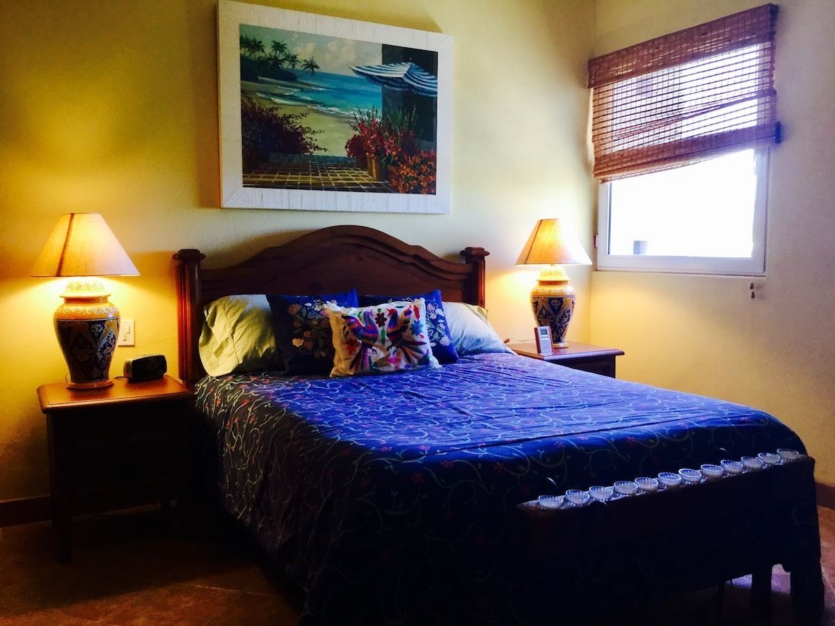 Une chambre à coucher avec un lit, deux tables de chevet avec des lampes, un tableau au mur et une fenêtre avec des stores.