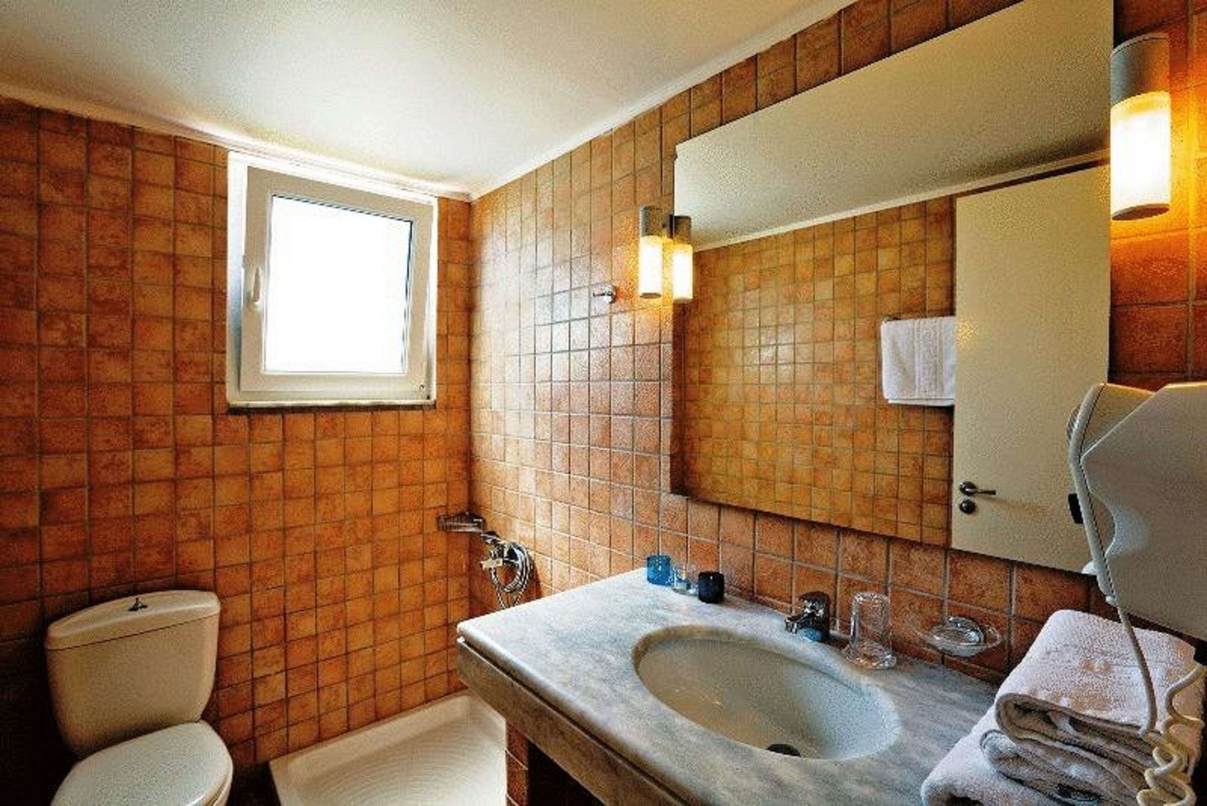 Casa de banho com parede revestida em azulejos, pia, espelho, porta-toalhas e janela.