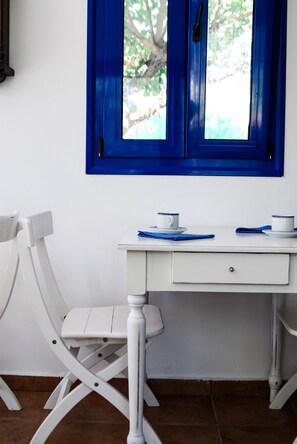 Un escritorio blanco con dos sillas blancas, una ventana con marco azul y una pared blanca.