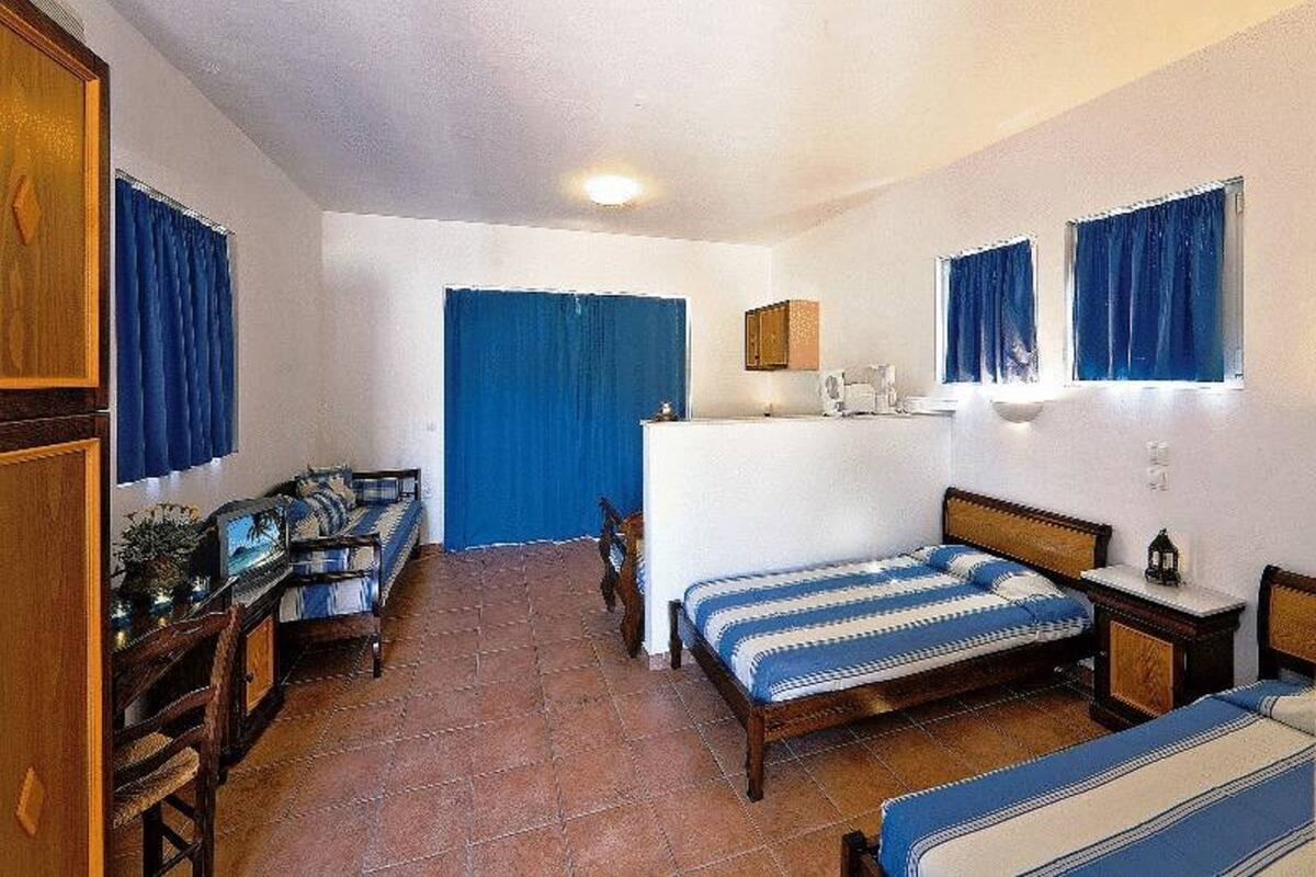 Una habitación con dos camas, un escritorio, una silla, una mesita y una ventana con cortinas.