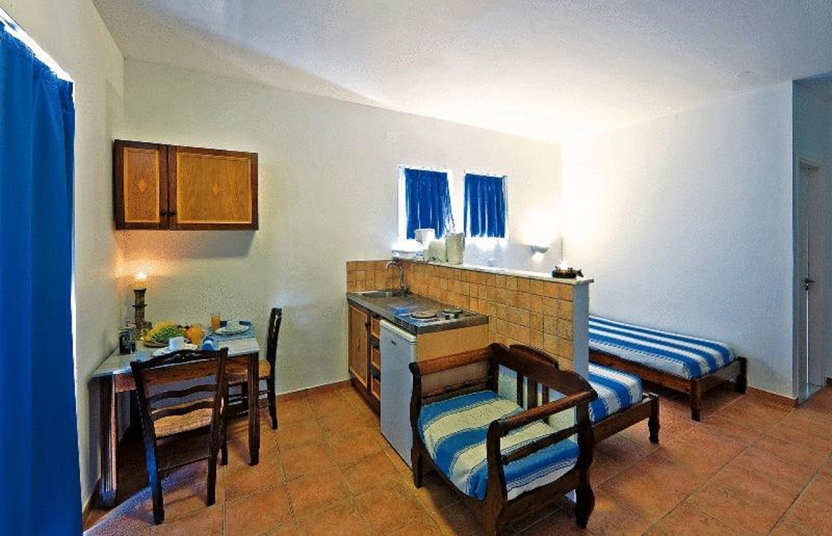 A compact room with a kitchenette, a dining table with chairs, and two single beds.