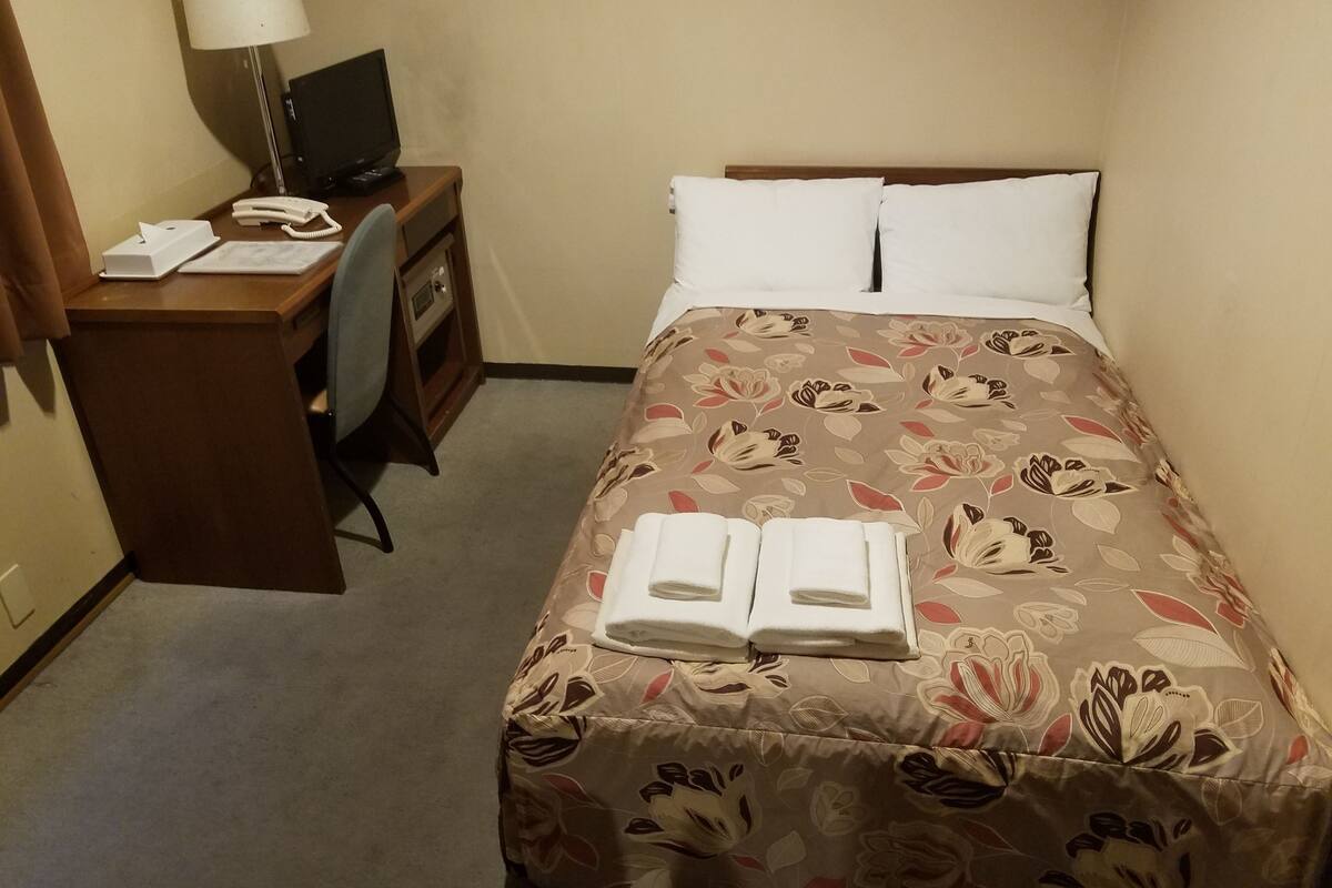 A hotel room with a bed, a desk, a chair, a lamp, and a telephone.