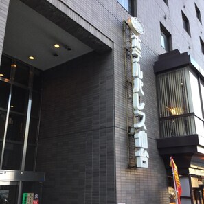 Fachada de edificio con un cartel grande en caracteres japoneses, diseño arquitectónico moderno y una bandera.