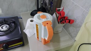 Una cucina con piano cottura a gas, macchina del caffè e un contenitore con utensili rossi e neri.