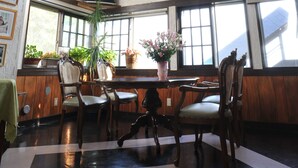 A dining area with wooden furniture, large windows, and hanging lights. - Petit Hotel Paddington House (Yamanouchi)