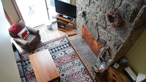 Un salón acogedor con chimenea de piedra, un sillón de cuero, una mesa de centro de madera y una alfombra estampada.